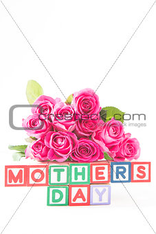 Bouquet of pink roses next to wooden blocks of different colours spelling mothers day