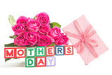 Bouquet of pink roses and pink gift next to wooden blocks of different colours spelling mothers day