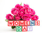 Bunch of pink roses next to wooden blocks spelling womens day