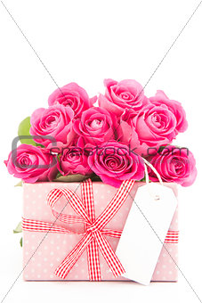 Bouquet of beautiful pink roses next to a pink gift with a blank card on white background
