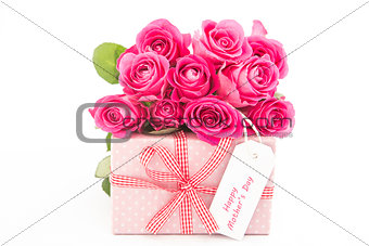 Bouquet of pink roses next to a pink gift with a happy mothers day card on white background