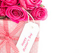Close up of a bouquet of pink roses next to a pink gift with a happy mothers day card on a white bac