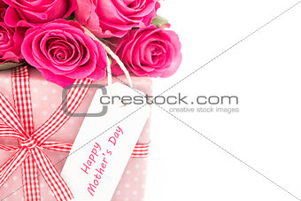 Close up of a bouquet of pink roses next to a pink gift with a happy mothers day card on a white bac