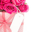 Close up of a bouquet of pink roses next to a pink gift with a blank card on a white background