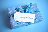 Pretty blue gift with a happy birthday card on a blue background
