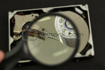 Hand holding magnifying glass over disk drive