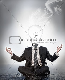 Businessman with bulb head sitting in meditation position