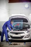 Man repairing car with open hood and small futuristic interface