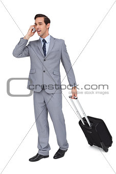 Smiling young businessman with his luggage while phoning