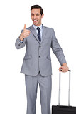 Smiling businessman with suitcase showing his thumb up
