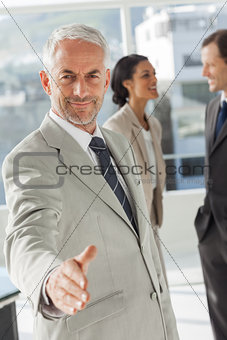 Businessman giving a handshake with colleagues behind