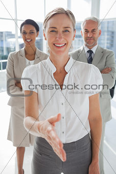 Smiling businesswoman giving a handshake with colleagues behind