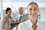 Cheerful businesswoman standing with colleagues working behind