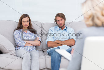 Upset couple sit on a sofa with arms crossed