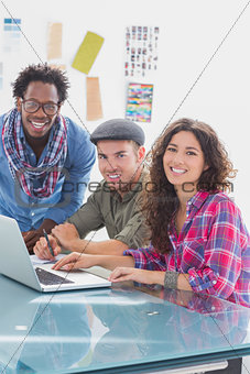 Creative team working together on laptop and smiling at camera