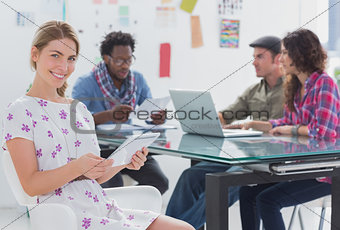 Editor holding tablet and smiling as team works behind her