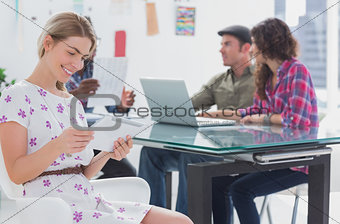Editor holding tablet and smiling as her team works behind her