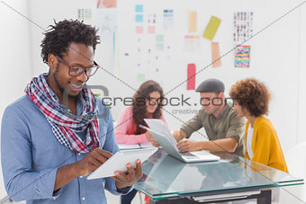 Smiling man using tablet with creative team working behind