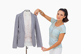 Fashion designer measuring blazer sleeve on mannequin and looking at camera