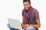 Smiling man sitting on floor using laptop looking at camera