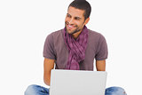 Fashionable man sitting on floor using laptop and looking away