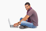 Fashionable man sitting on floor using laptop smiling at camera