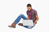 Smiling man wearing scarf sitting on floor using laptop