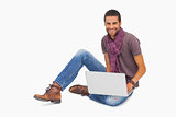Happy man wearing scarf sitting on floor using laptop