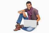 Happy man sitting on floor using laptop looking at camera