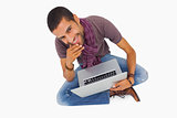 Thoughtful man sitting on floor using laptop and smiling at camera