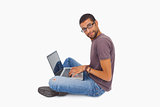Man wearing glasses sitting on floor using laptop and looking at camera