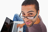 Man wearing glasses sitting on floor using laptop and smiling up at camera