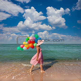 Young woman walking on the beach with colored balloons / Travel