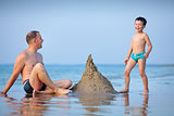 Young father and his little son building sand castle at beach