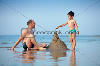 Young father and his little son building sand castle at beach