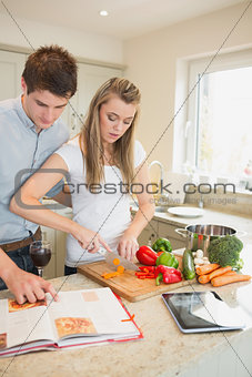 Woman chopping peppers with man reading cookbook