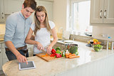 Woman cutting vegetables with man using tablet computer