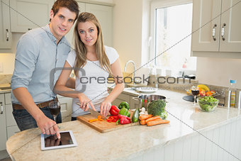 Man pointing on tablet pc with woman chopping peppers