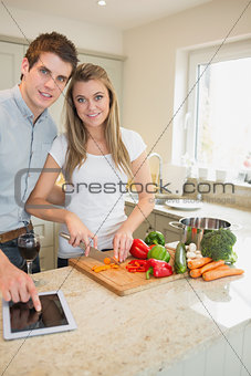 Woman chopping peppers with man typing on the tablet pc