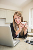 Woman drinking a beverage while working on laptop