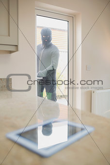 Burglar looking at tablet pc through kitchen door