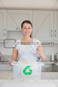 Smiling woman throwing bottle into recycling bin
