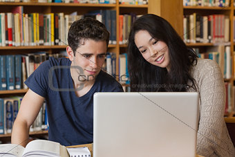 Two students learning in a library with a laptop