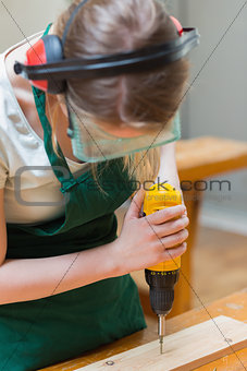 Student drilling a hole in a wooden board at the workbench