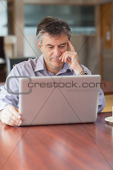 Man using a laptop in a coffee shop and thinking