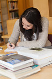 Student sitting in a library at a desk and writing
