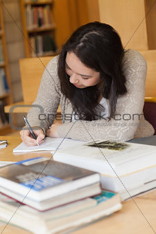 Student sitting in a library at a desk and writing