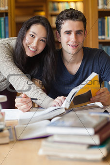 Two students studying at a desk in a library