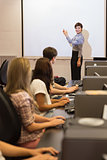 Computer class looking at teacher pointing on projection screen