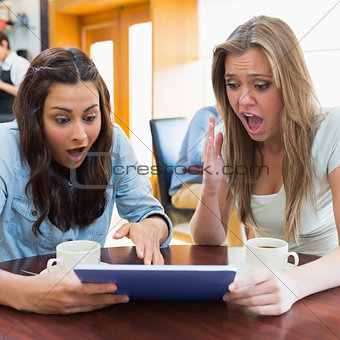 Women looking shocked at tablet pc in canteen